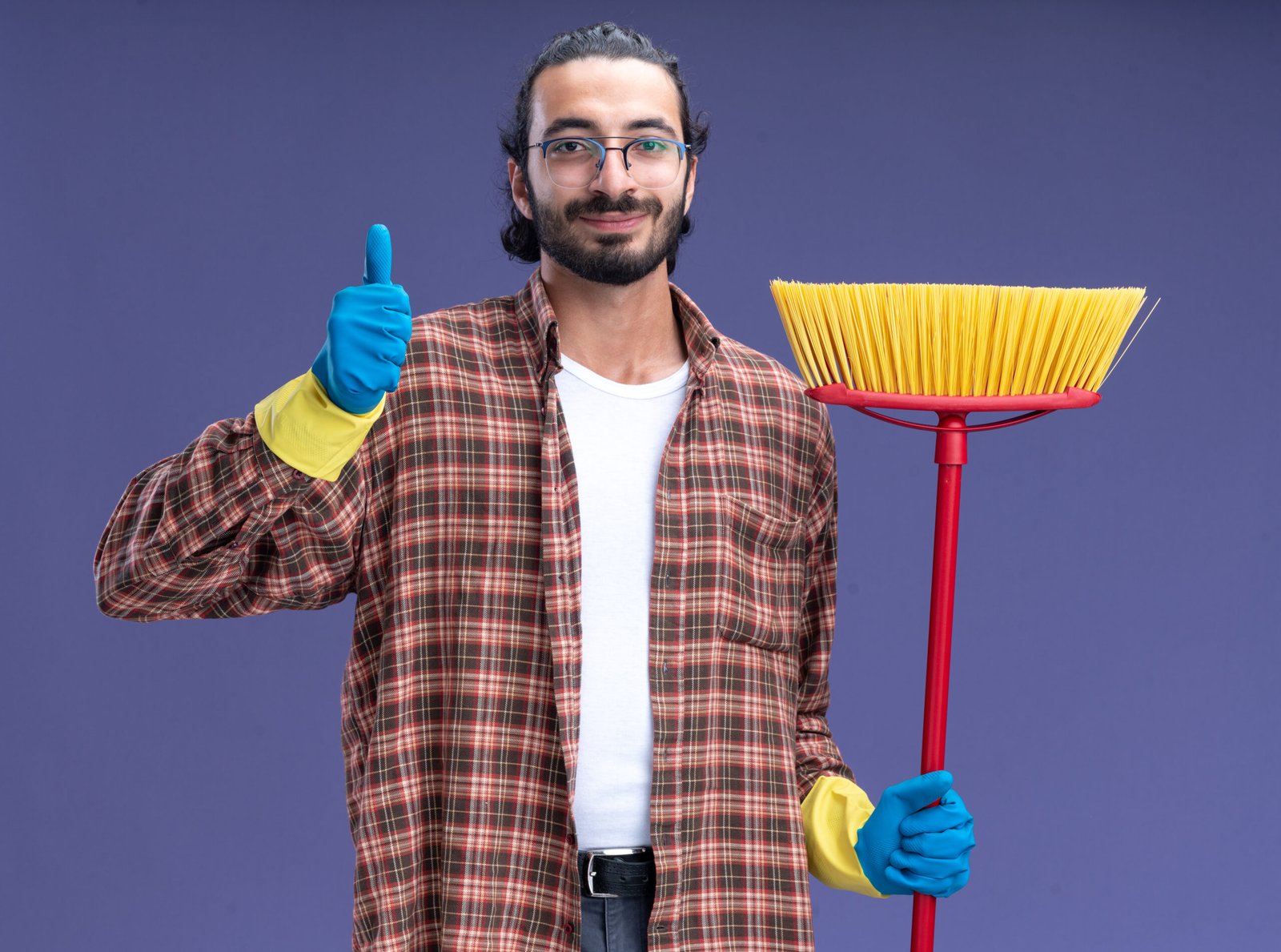 Homem jovem com uma vassoura sorrindo e com o polegar para cima